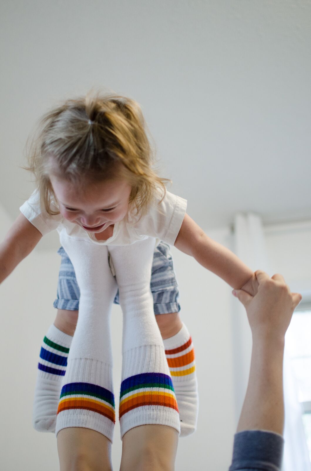 Person wearing rainbow under the knee socks from 6 pack collection worn by mom and son playing on bed