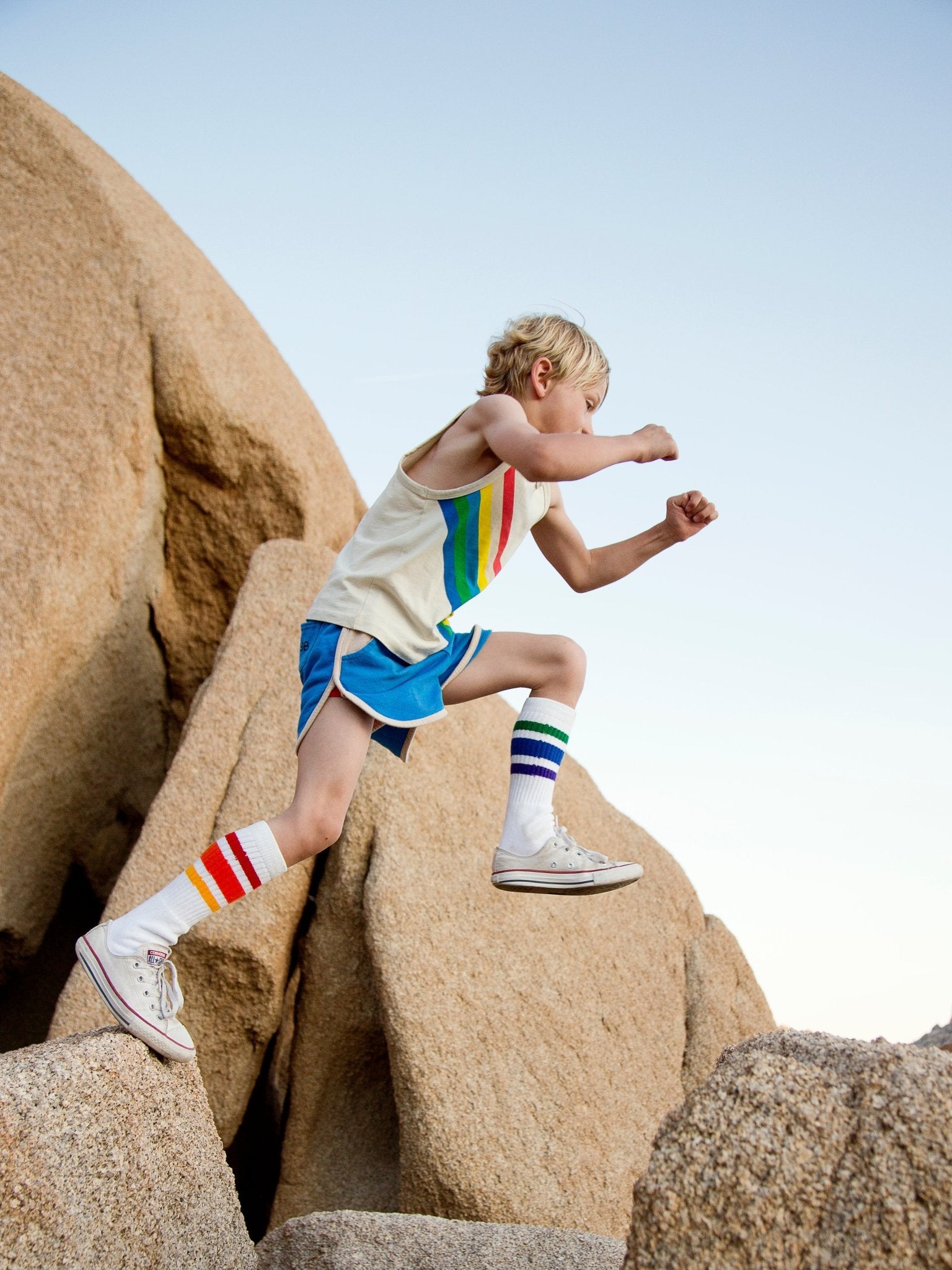 Kid wearing Courage rainbow tube socks while playing outside jumping from one rock to another