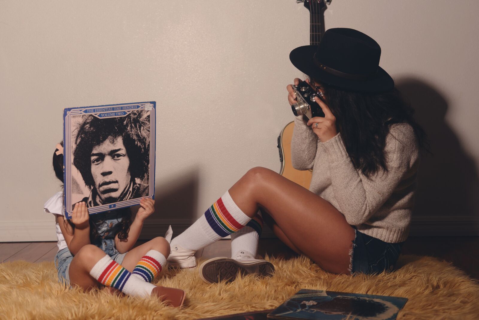 Two people sitting on a carpet with a guitar and a photo album.