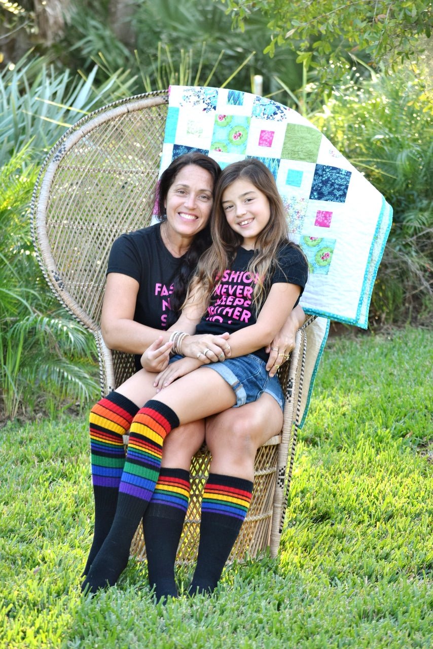 Person wearing Power rainbow knee high socks outdoors with mom and daughter sitting on a chair.