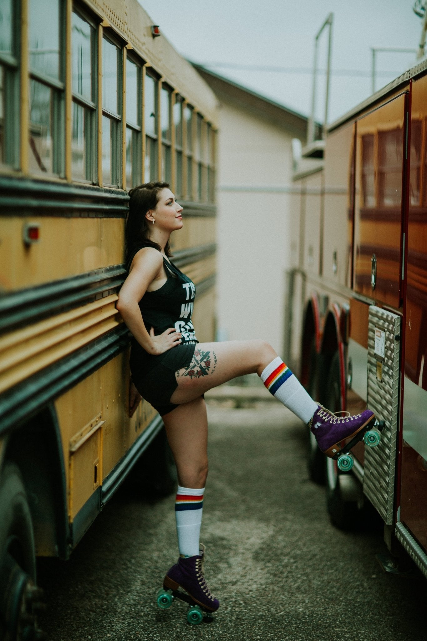 Person wearing Love rainbow knee high tube socks outdoors with roller skates on by the school bus