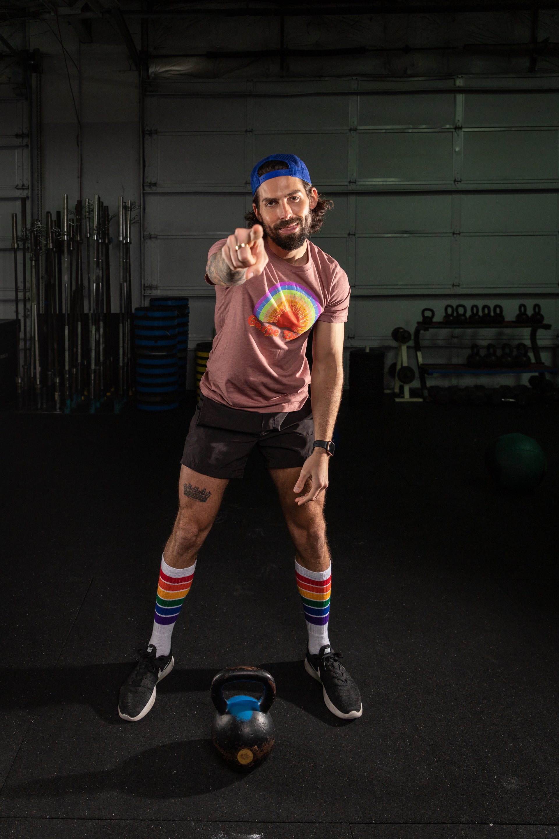 Man in a gym pointing at the camera with colorful socks and a tie-dye shirt.